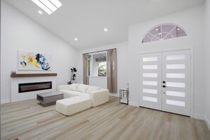 Una sala de estar moderna con chimenea, un sofá, una mesa de centro y un ventanal con cortinas.
