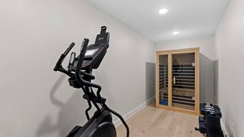 Una habitación con una bicicleta estática, una puerta de madera con paneles de vidrio e iluminación empotrada en el techo.