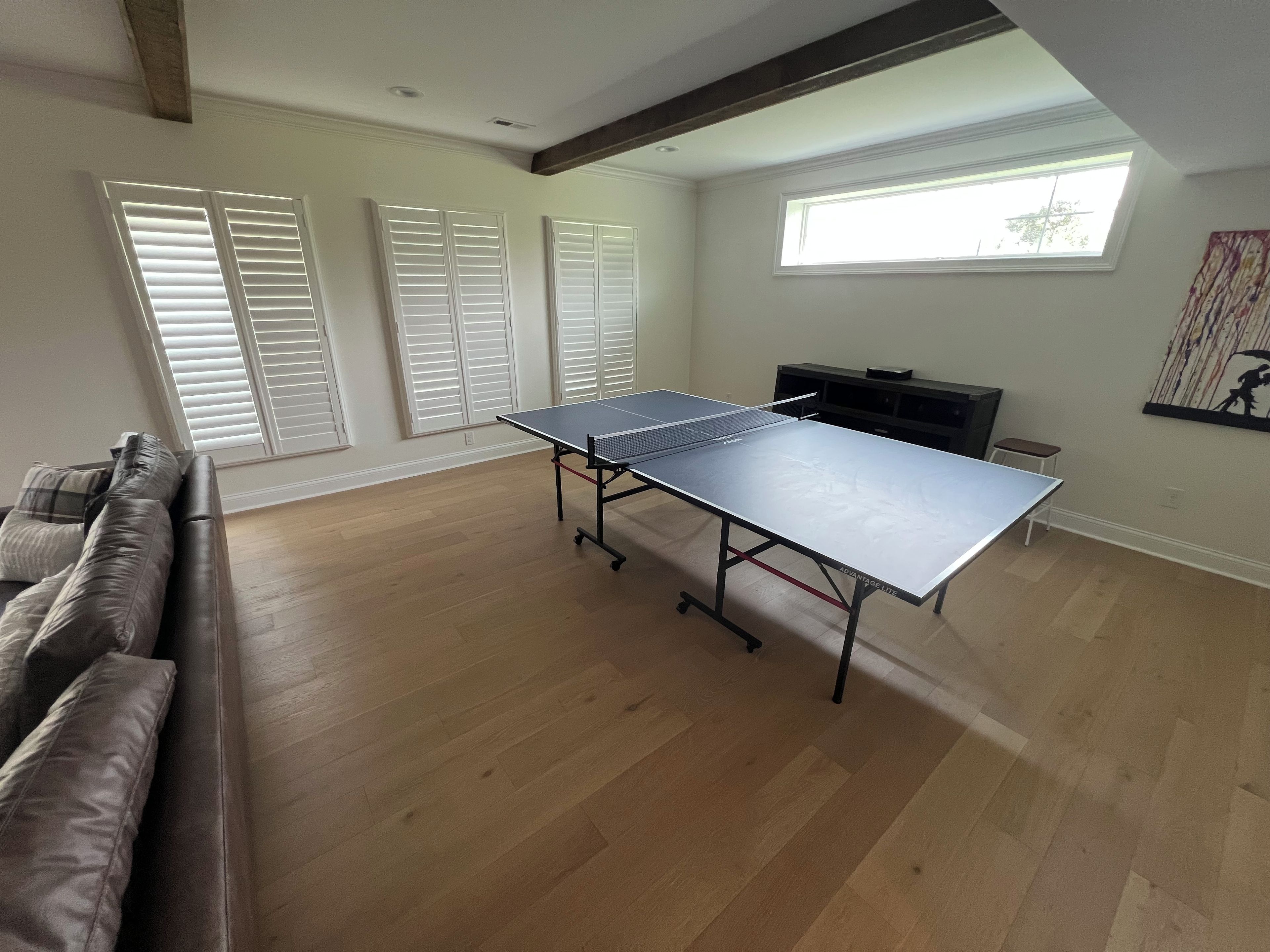 A room with a ping pong table, a sofa, and a window with blinds.