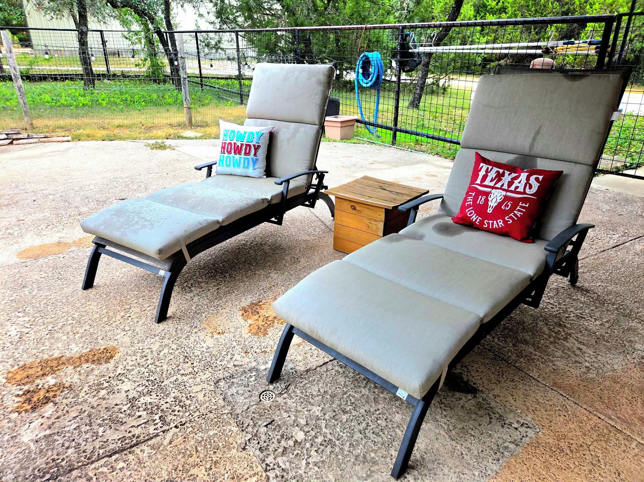 Zwei Loungestühle mit Kissen, einer mit einem 'Howdy'-Kissen und der andere mit einem 'Texas Lone Star'-Kissen, auf einer Beton-Terrasse mit einem Zaun im Hintergrund.