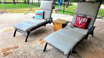 Zwei Loungestühle mit Kissen, einer mit einem 'Howdy'-Kissen und der andere mit einem 'Texas Lone Star'-Kissen, auf einer Beton-Terrasse mit einem Zaun im Hintergrund.