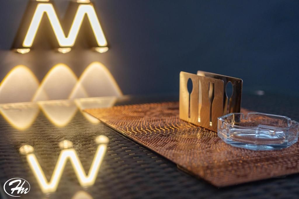A textured surface with a clear glass ashtray and a metal object with cut-out shapes.