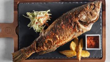 A whole grilled fish with a side of coleslaw and wedges on a slate serving board.
