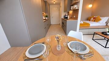 A dining area with a table set for two, a kitchen in the background, and a living area with a sofa and cushions.