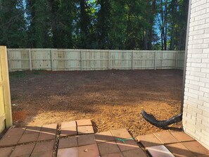 Une cour arrière avec une clôture en bois, un mur de briques et un tuyau d’arrosage.