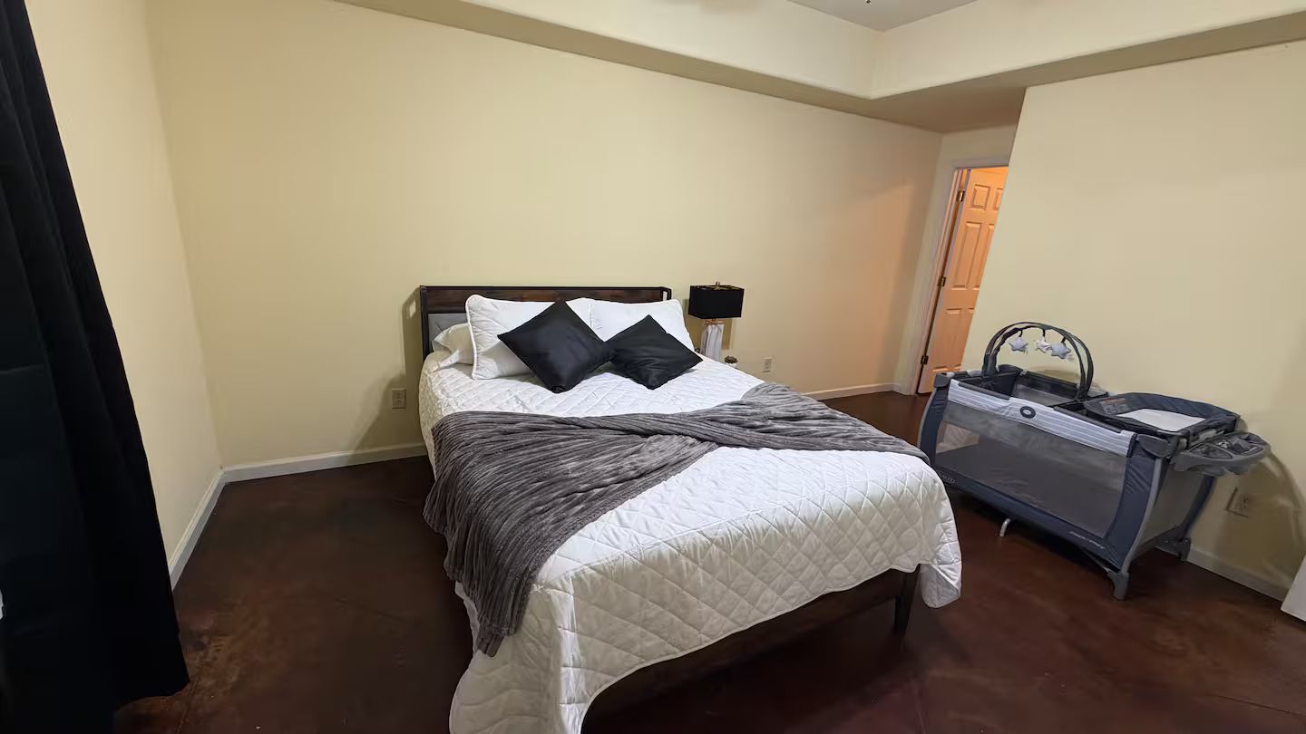 A bedroom with a bed, a nightstand, a treadmill, and a door leading to another room.