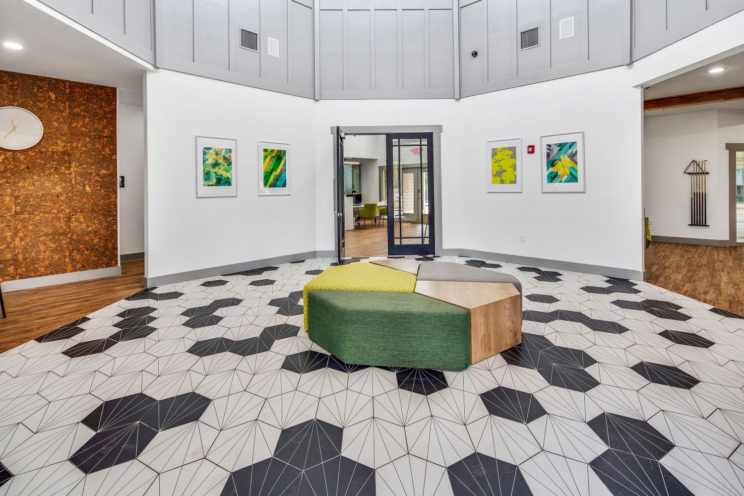 A spacious lobby with a geometric patterned floor, a green and wooden seating area, and artwork on the walls.