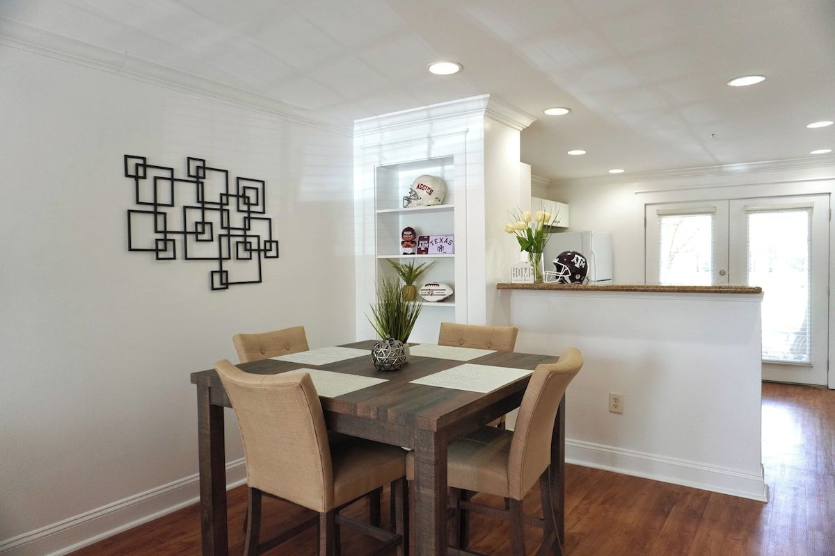 A dining area with a wooden table and chairs, a decorative wall piece, and a shelf with sports memorabilia.