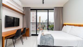 Habitación de hotel con cama, escritorio, silla, televisor y balcón con vista a la ciudad.