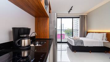 A modern hotel room with a kitchenette, a bed, and a balcony with a city view.