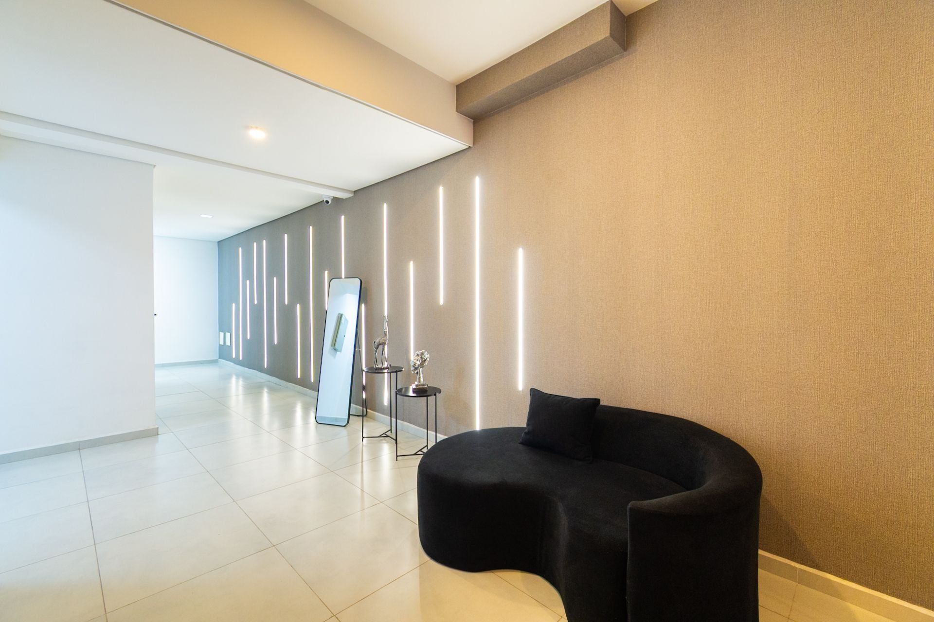 A modern hotel lobby with a curved black seating area, a large mirror, and a decorative sculpture on a small table.