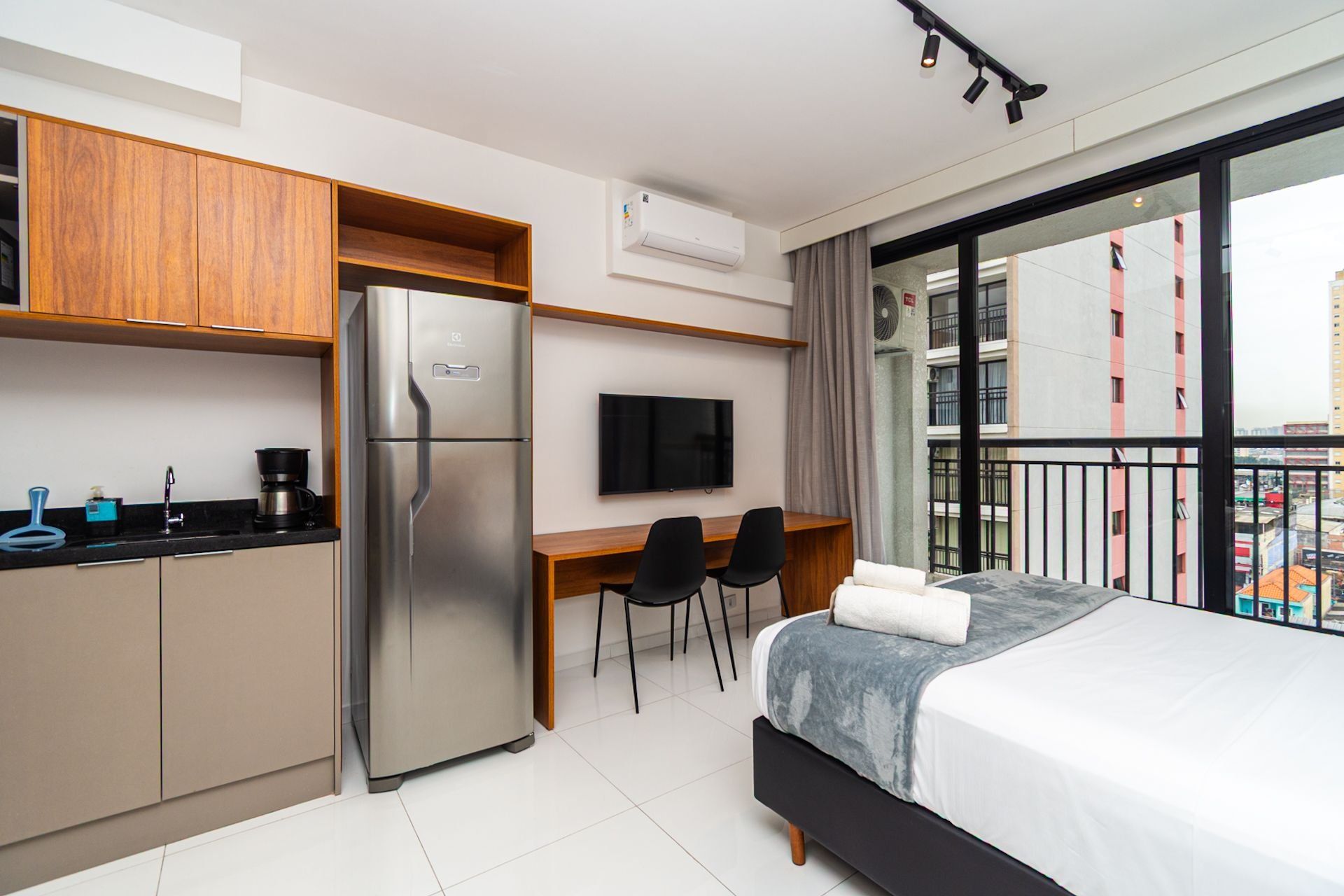 Une chambre d’hôtel moderne équipée d’une kitchenette, d’un lit, d’une télévision et d’un balcon offrant une vue sur la ville.