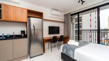 Une chambre d’hôtel moderne équipée d’une kitchenette, d’un lit, d’une télévision et d’un balcon offrant une vue sur la ville.