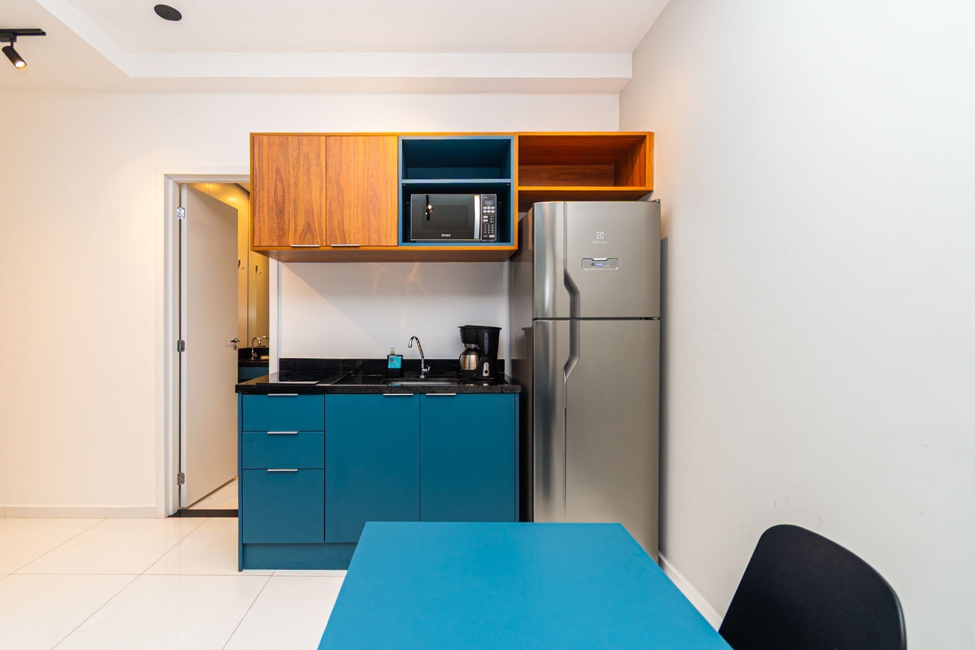 A compact kitchen with a microwave, refrigerator, and a blue table.
