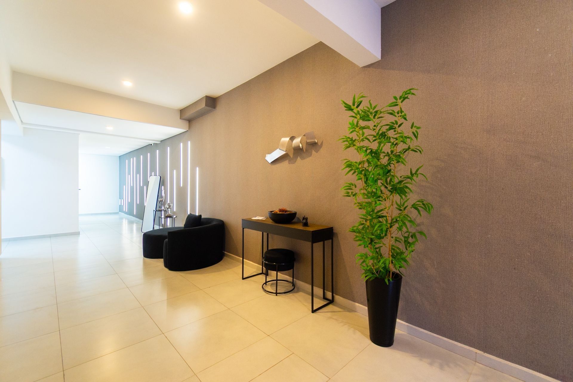 Un intérieur moderne agrémenté d’une grande plante en pot, d’un coin salon avec une table et d’un luminaire fixé au mur.