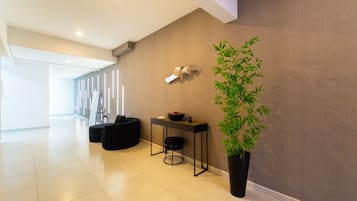 Un intérieur moderne agrémenté d’une grande plante en pot, d’un coin salon avec une table et d’un luminaire fixé au mur.