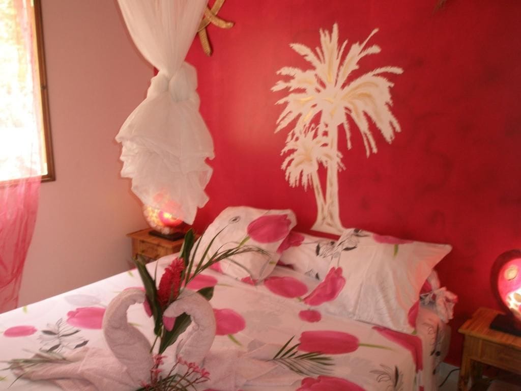 A bedroom with a bed, a nightstand, a lamp, and a wall with a palm tree design.