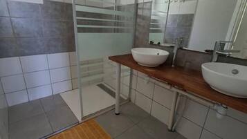 Un baño con cabina de ducha de vidrio, dos lavamanos y un espejo grande.