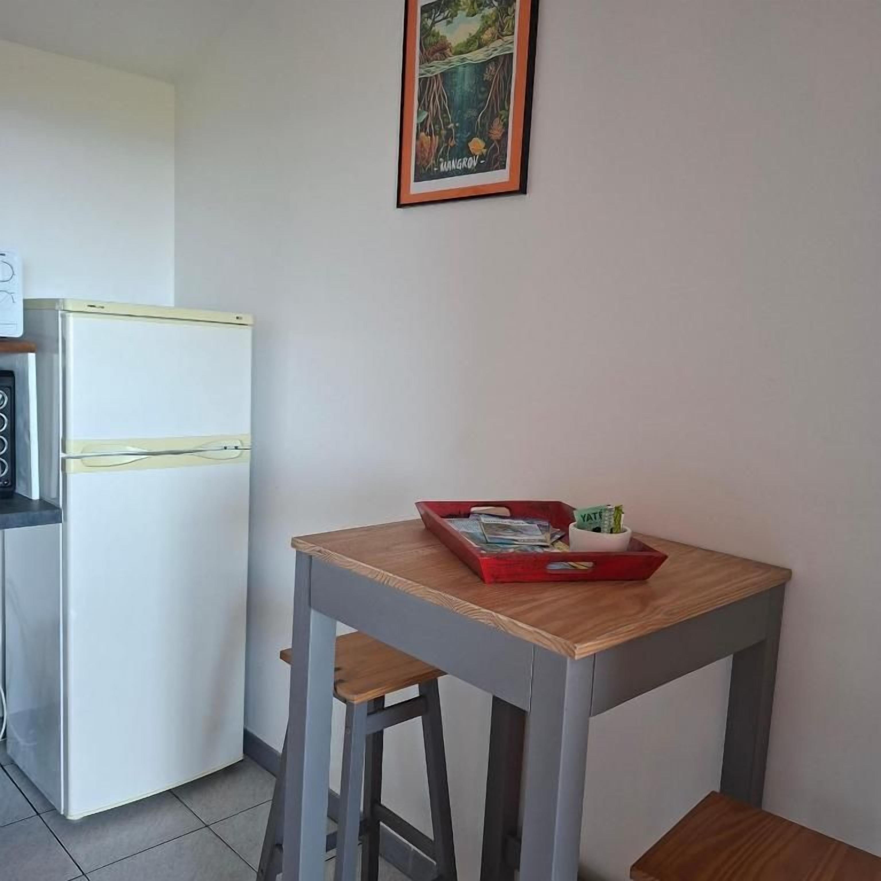 A compact kitchen with a refrigerator, a small table with a tray, and a framed picture on the wall.
