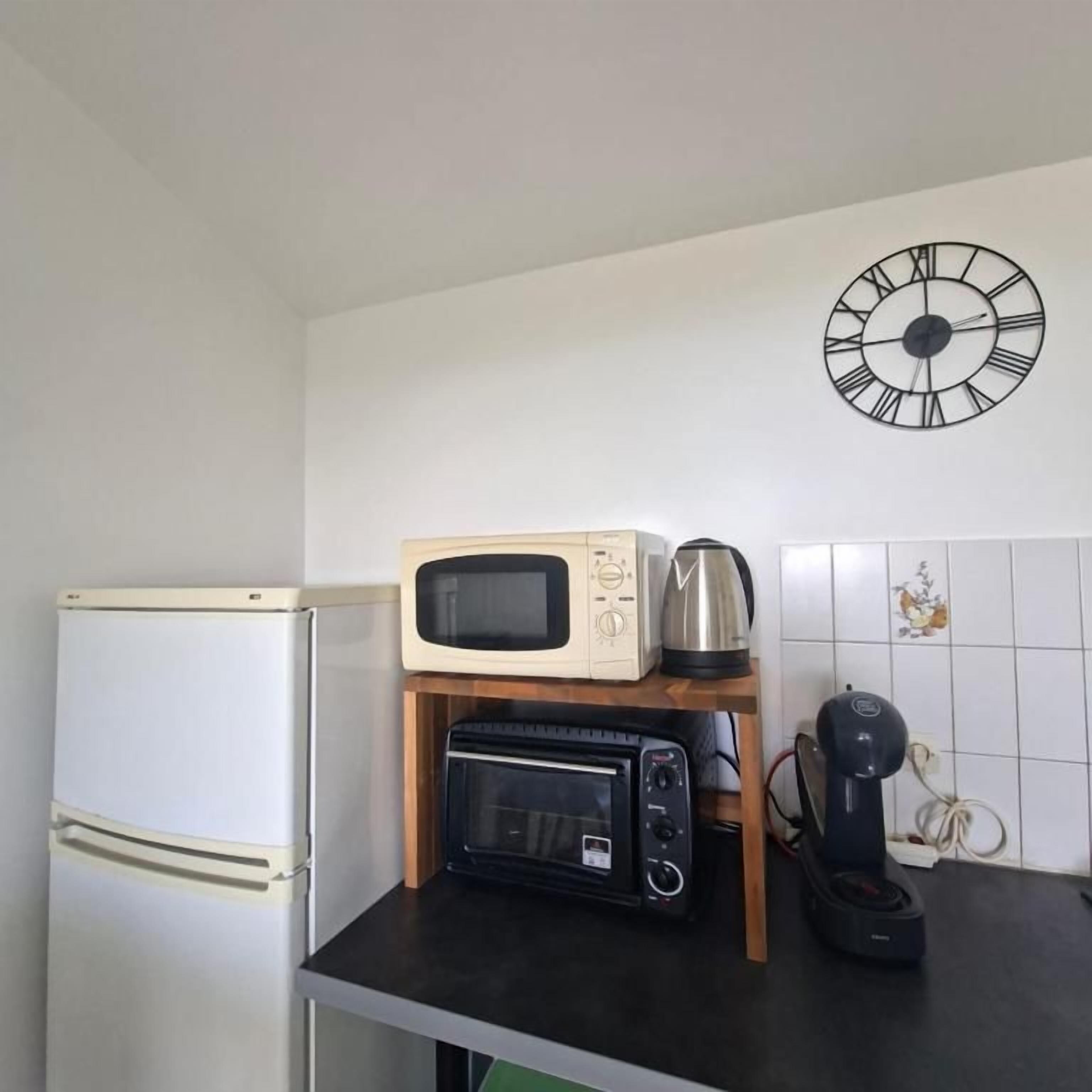 Ett kök med ett vitt kylskåp, en mikrovågsugn, en liten ugn med grillfunktion och en kaffebryggare placerade på en bänkskiva.