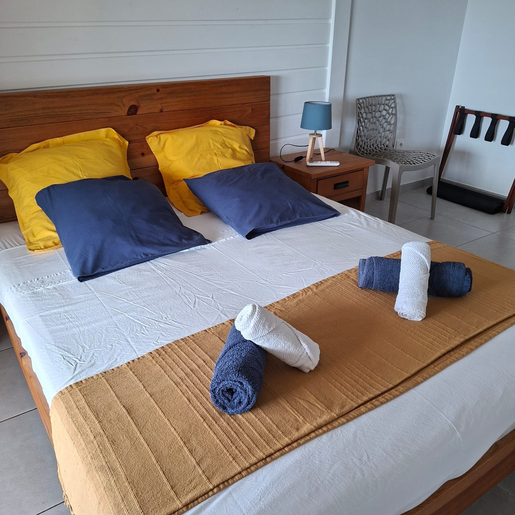 A neatly made bed with a brown blanket, two pillows, and rolled towels.