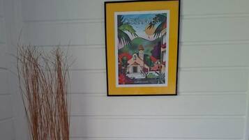 A framed picture of a village scene, a tall decorative plant, and a tray with cups and a teapot on a wooden table.