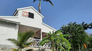 A white building with a balcony, surrounded by palm trees and greenery.