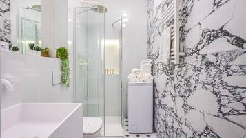 Un baño moderno con cabina de ducha de vidrio, un lavabo blanco y pared con estampado de mármol.