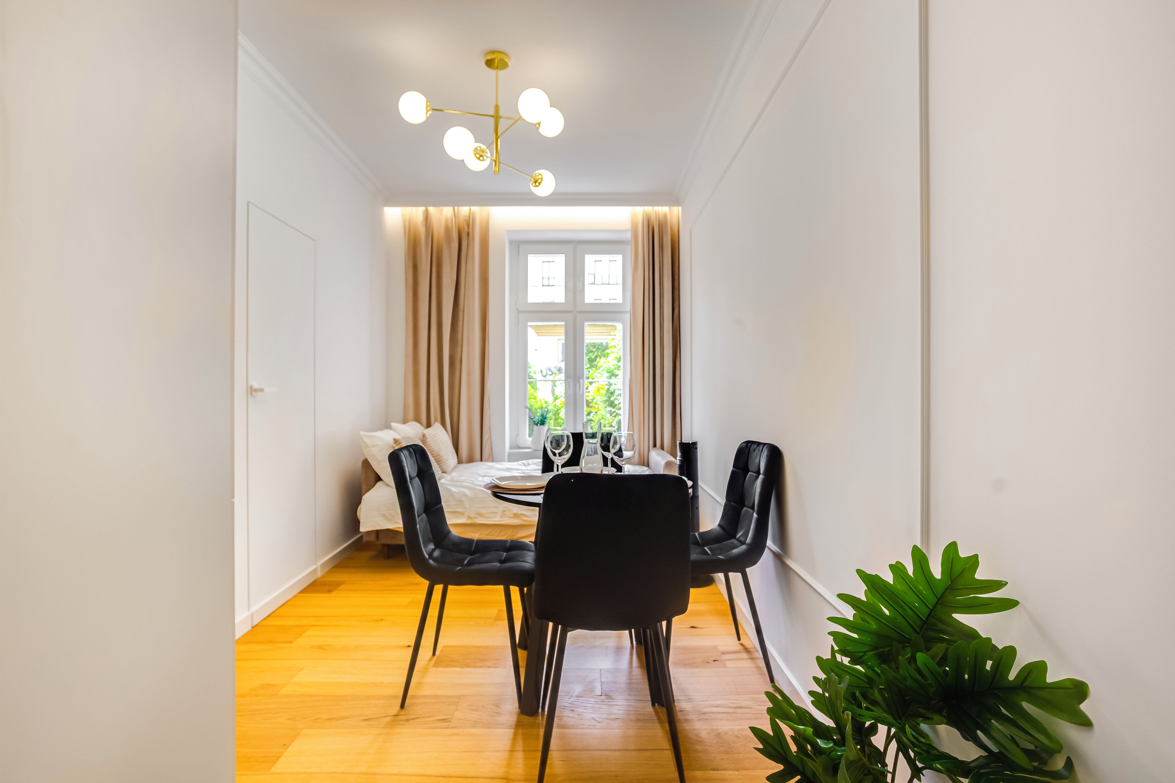 Habitación de hotel pequeña con cama, una mesa de comedor con sillas, un candelabro y vistas al verdor exterior.