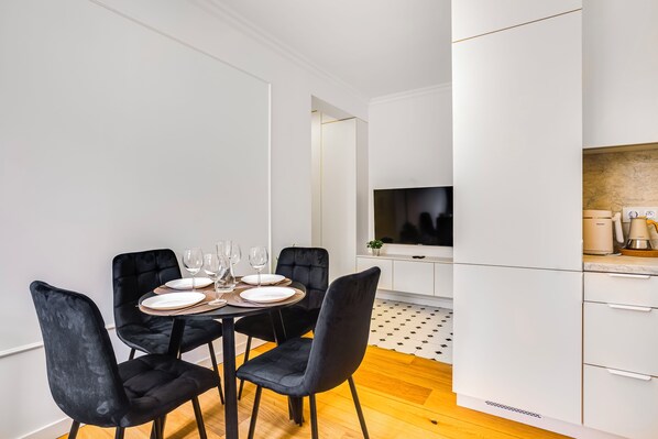 A modern dining area with a table set for four, black chairs, and a kitchen with white cabinets and a large screen. - Szmaragd & Grafit 5 min od Starego Rynku (Poznań)
