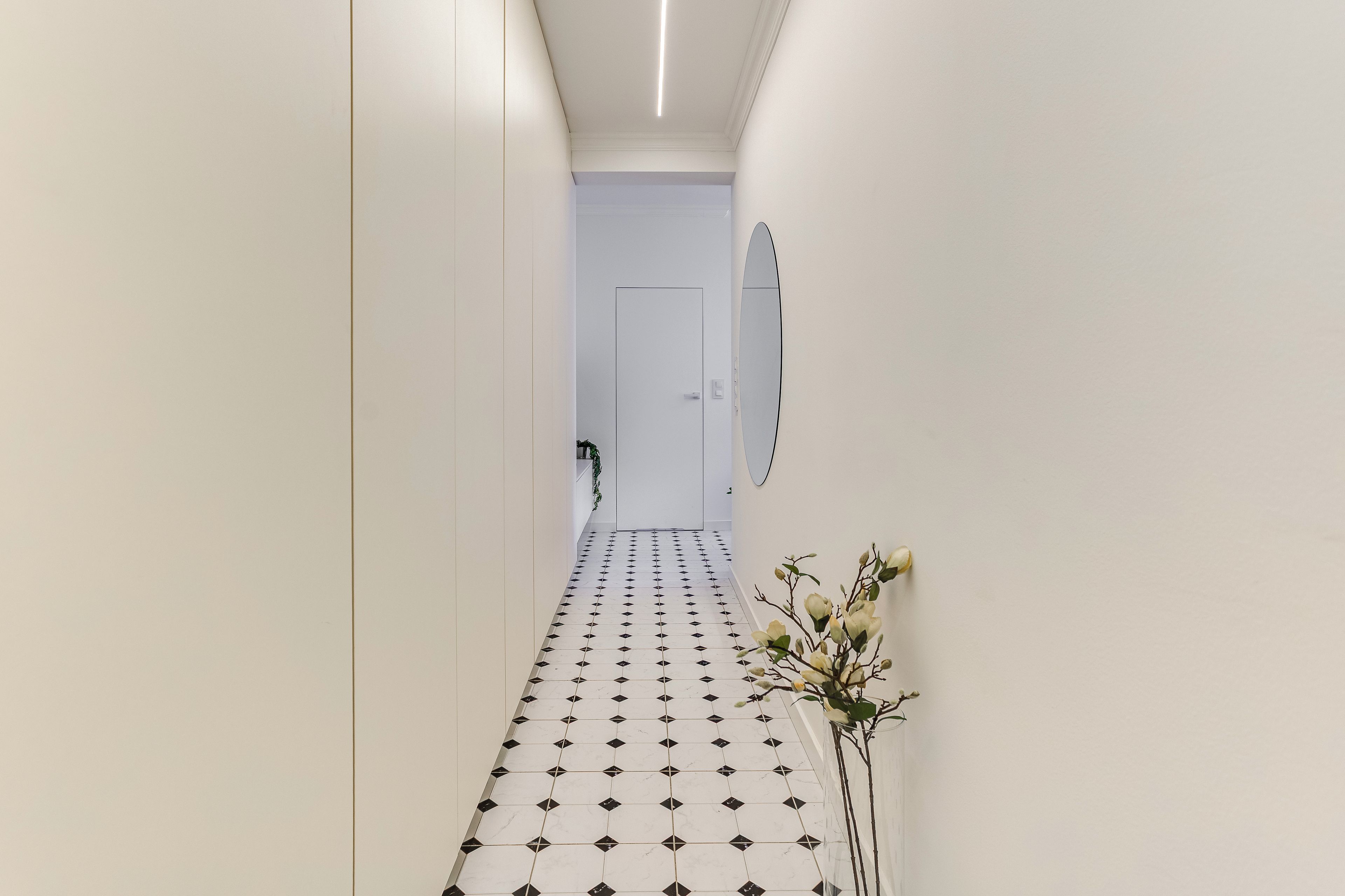 A hallway with a tiled floor, a door at the end, and a wall-mounted mirror.