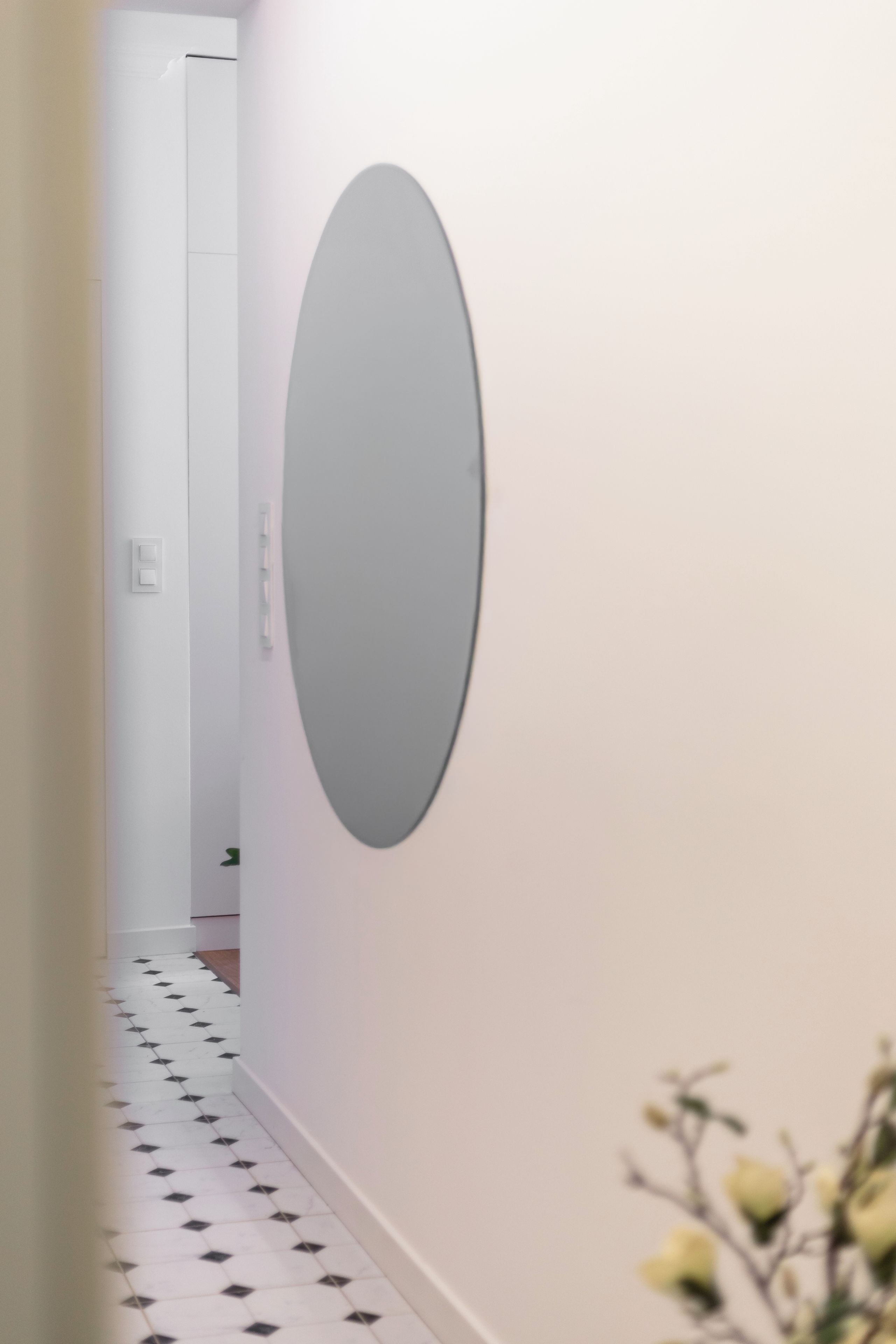 Un pasillo con piso blanco, un espejo grande en la pared y una puerta al final.