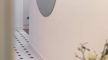Un pasillo con piso blanco, un espejo grande en la pared y una puerta al final.