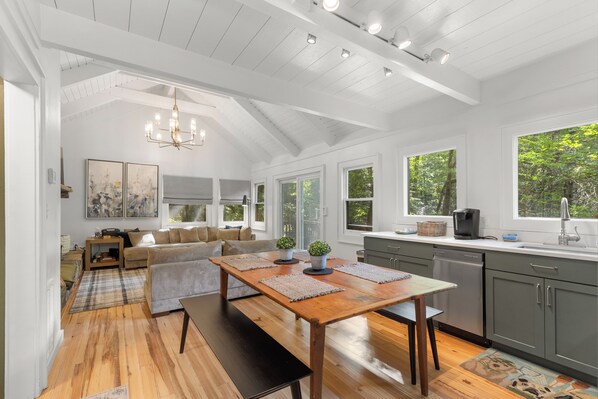 A spacious kitchen with a wooden table, a dining area with a sofa, and a view of the outdoors through large windows. - Ski Pet Friendly 3BR w/ Deck + Resort Access (Sapphire)