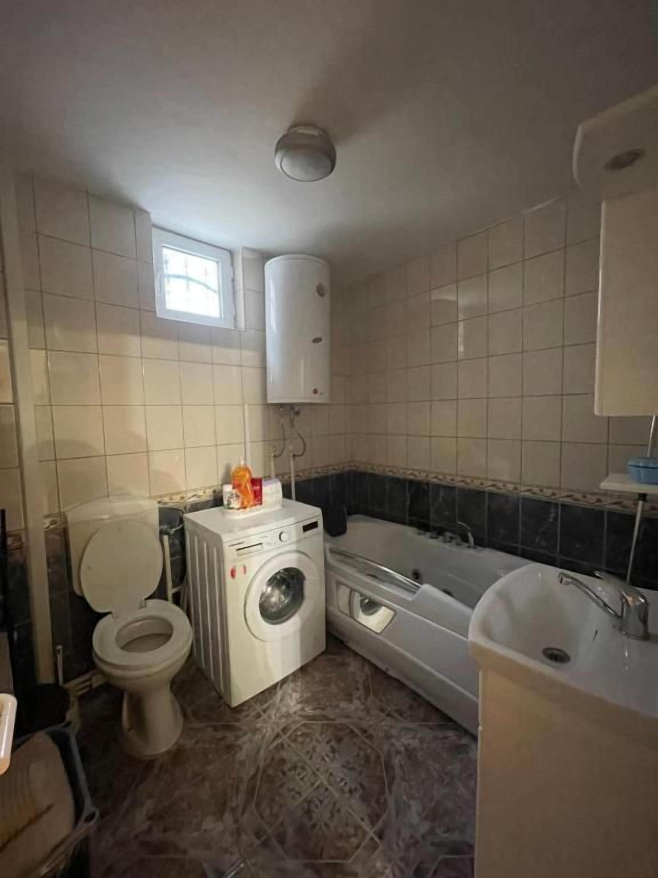 Casa de banho com sanita, máquina de lavar roupa, banheira e lavatório.