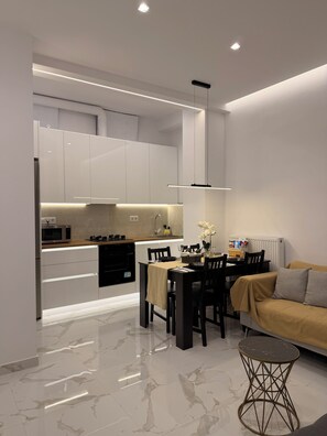 A modern kitchen with integrated appliances, a dining area with a table and chairs, and a living space with a sofa and a coffee table. - The Oasis luxury apartment in Athens (Moschato)