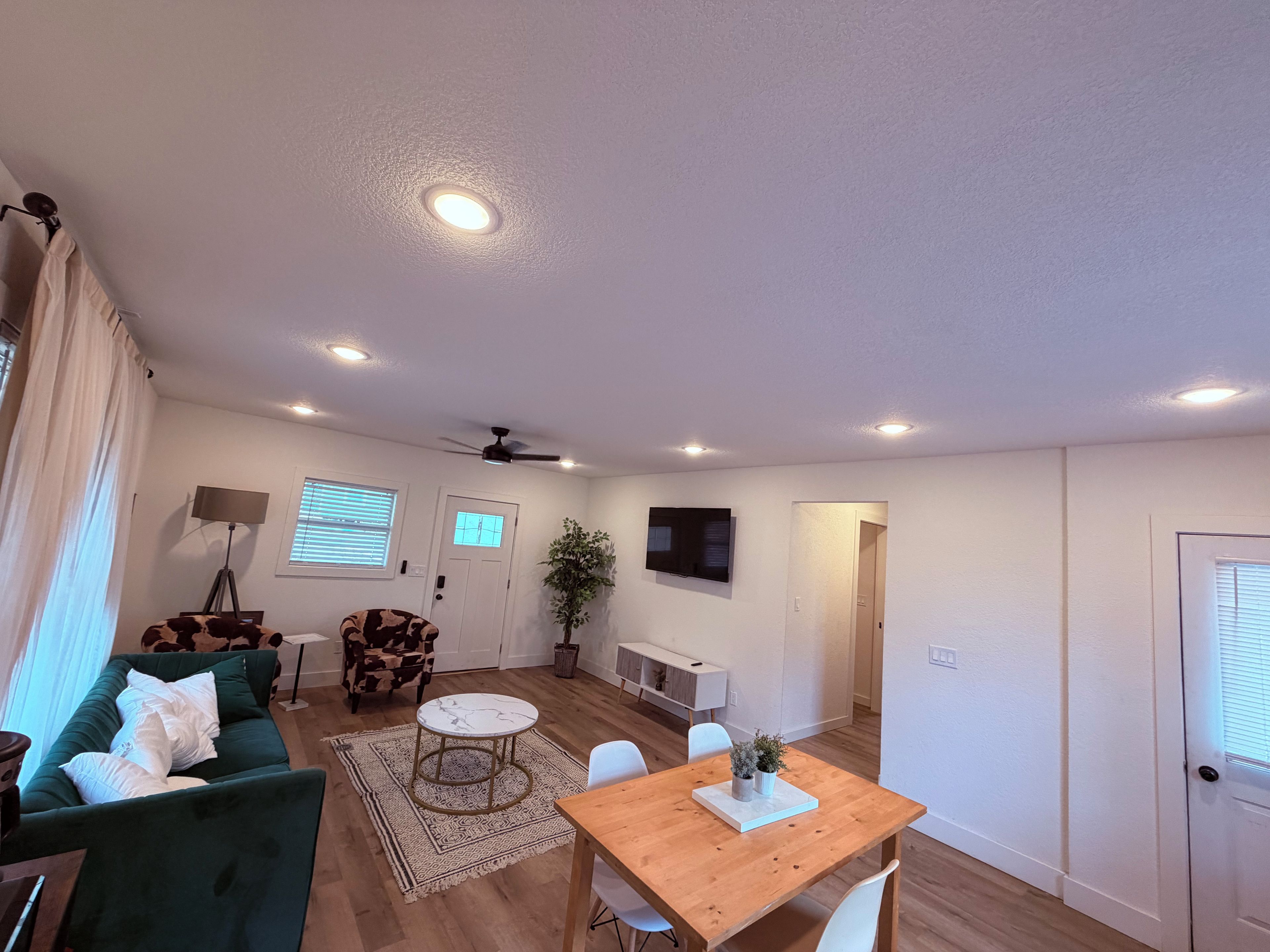 Un salon moderne avec un canapé vert, une table à manger en bois et un ventilateur de plafond.