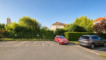 Un parking avec deux voitures, un bâtiment avec un toit rouge et, au loin, le clocher d’une église.