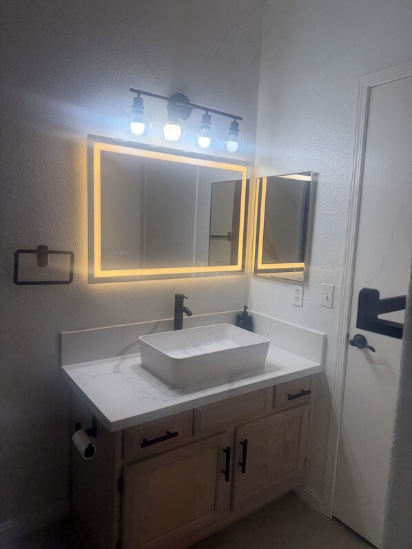 A bathroom with a white vanity, a rectangular sink, a mirror with lights, and wooden cabinets. - 2-bed, 2-bath condo, guard-gated, pool, spa, and fitness center. (Las Vegas)