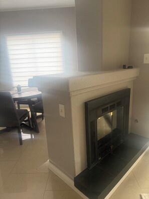 A living room with a fireplace, a dining area with chairs and a table, and a window with blinds. - 2-bed, 2-bath condo, guard-gated, pool, spa, and fitness center. (Las Vegas)