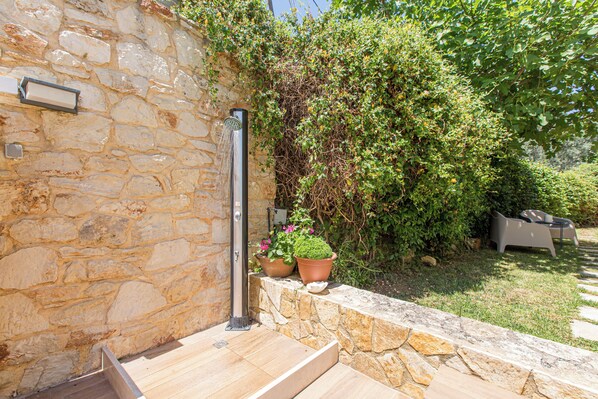 A stone wall with a metal water spout and steps leading to a garden area with potted plants and outdoor furniture. - Villa Armonia Boutique Living (Drakona)