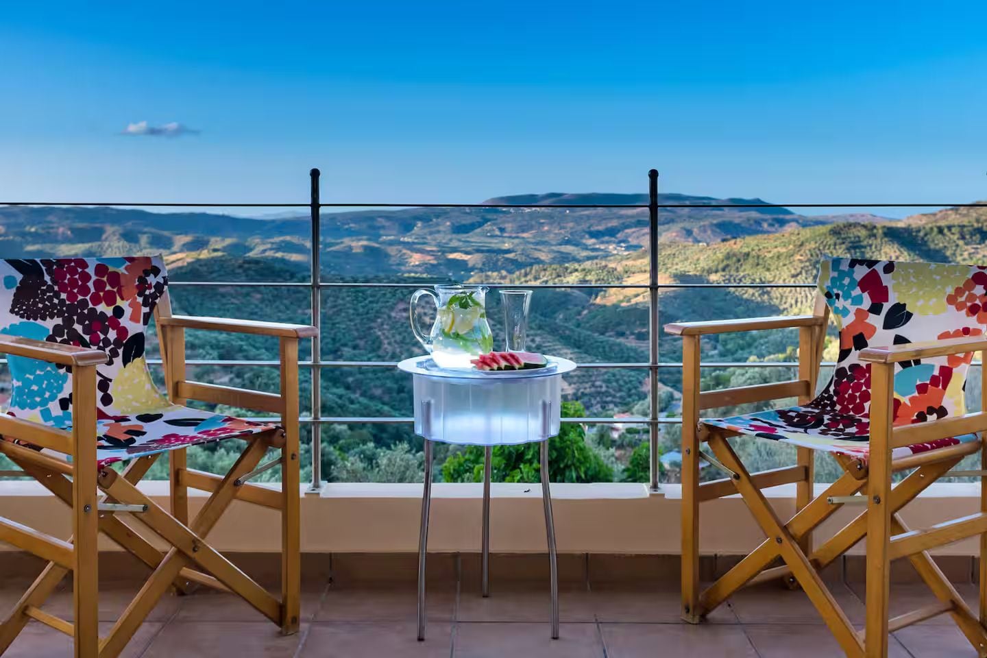A balcony with two wooden chairs and a table, overlooking a mountainous landscape.