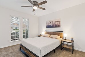 Un dormitorio con cama, mesita de noche, lámpara de pared, ventilador de techo y ventana con persianas.