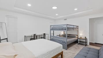 A modern bedroom with a bunk bed, a desk, a chair, and a sofa.