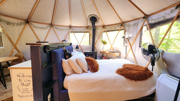 A cozy interior of a tent with a bed, a desk, a chair, and a table.