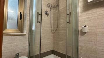 Un baño moderno con ducha envuelta en vidrio, lavamanos pedestal y retrete.