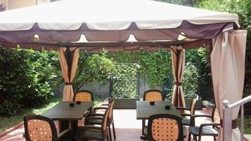 Un patio exterior con mesa y sillas bajo una pérgola.