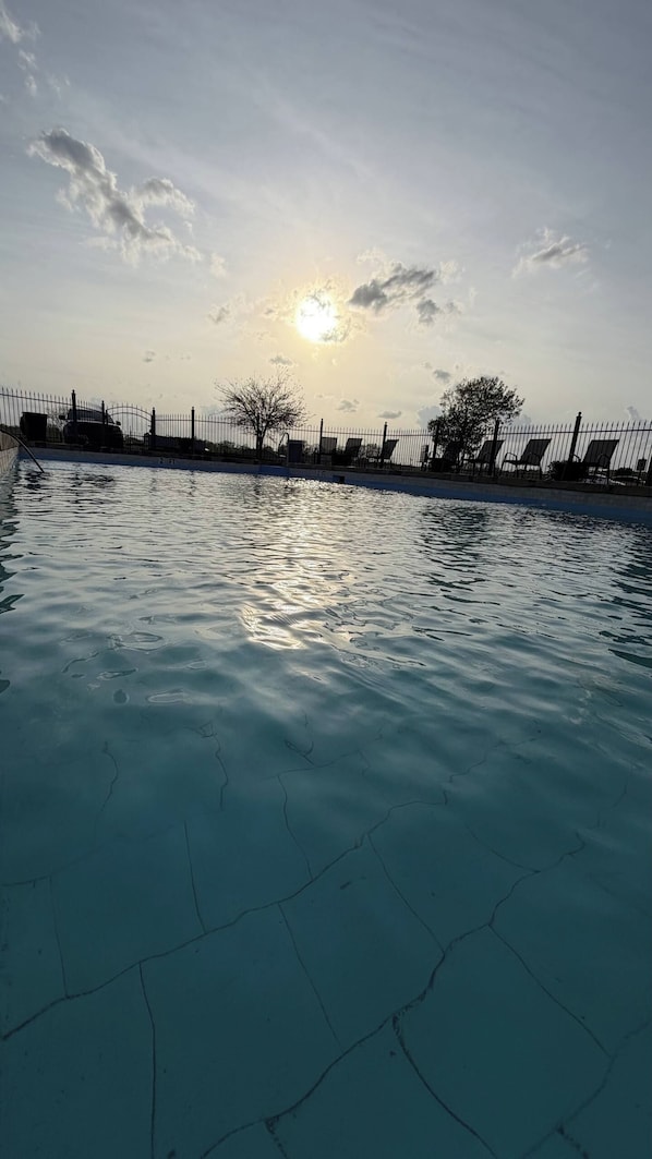 Una piscina con valla y sillas de descanso, bajo un cielo despejado con sol.