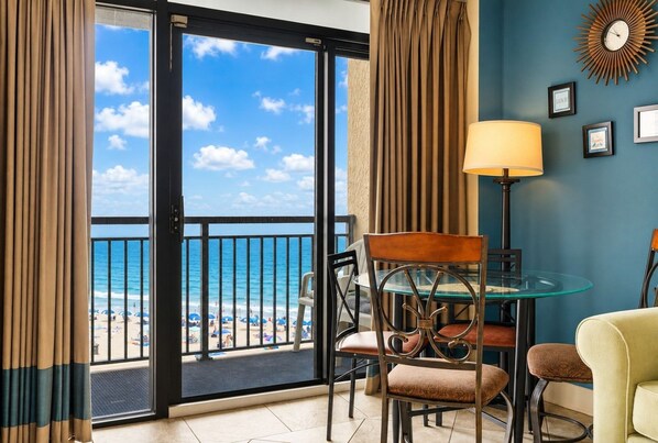 Golden lamp light warms this bright Beach Cove condo dining area, opening straight onto an oceanfront balcony with sweeping views. - Direct Oceanfront Balcony with Pools (North Myrtle Beach)