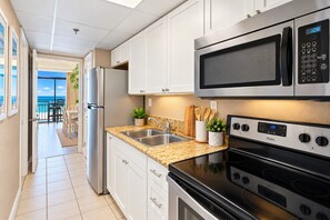 A modern kitchen with stainless steel appliances, a double sink, and a view to a balcony. - Caravelle Resort 1234 - Couples Oceanfront Escape with Pools and Hot tubs (Myrtle Beach)